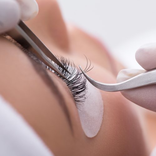 Close up of beautician hands sticking artificial eyelash to female eye